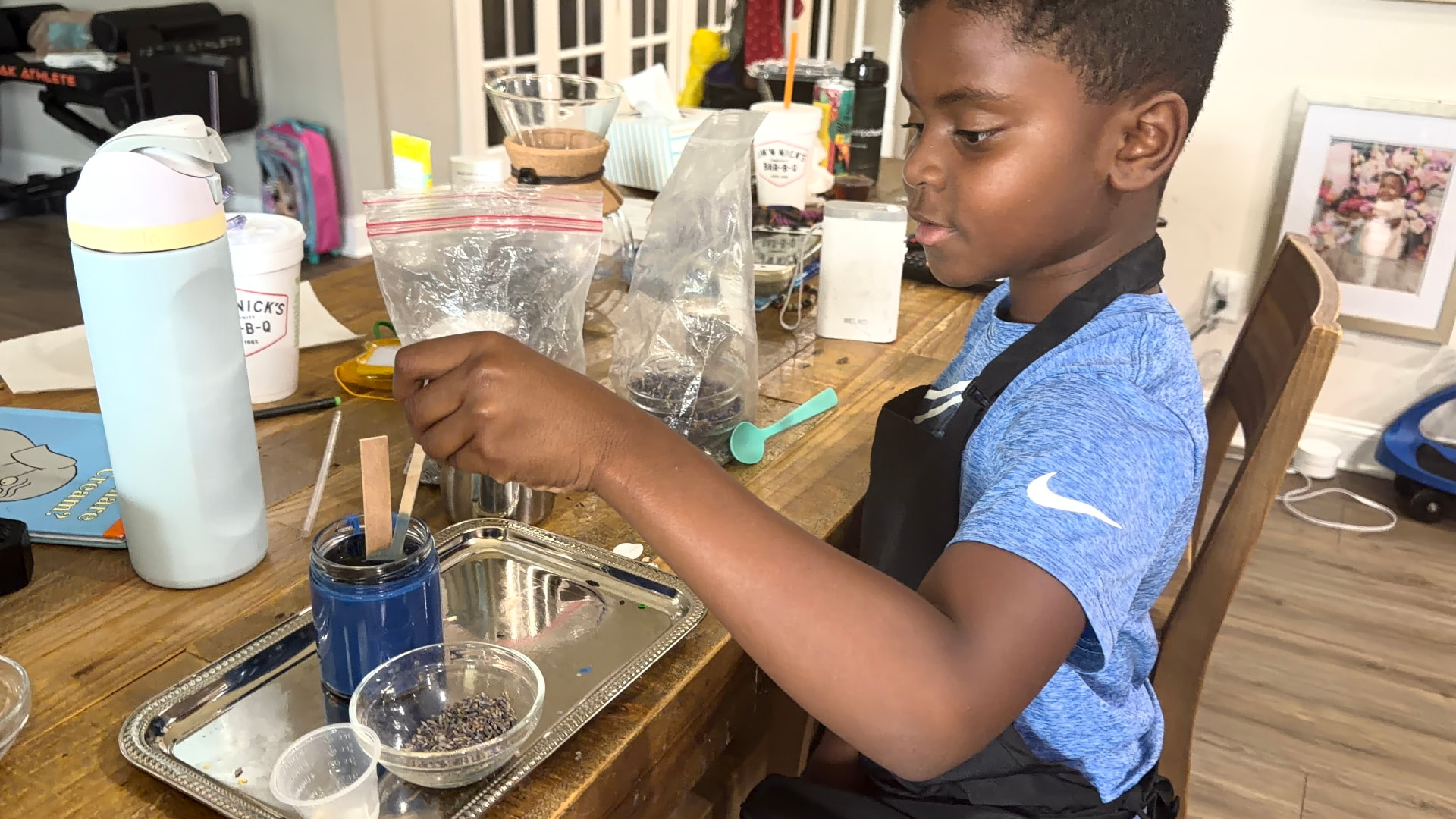 A young guest in an apron stirring his custom candle during a kids class